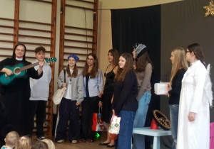 Siostra zakonna grająca na gitarze oraz młodzież w strojach galowych i kostiumach anioła podczas występu