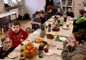 Uczniowie i nauczyciele przy wspólnym stole podczas wigilii klasowej z poczęstunkiem.